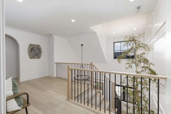 Hardwood flooring, recessed lighting, archway, black metal baluster railing, and a window with black trim