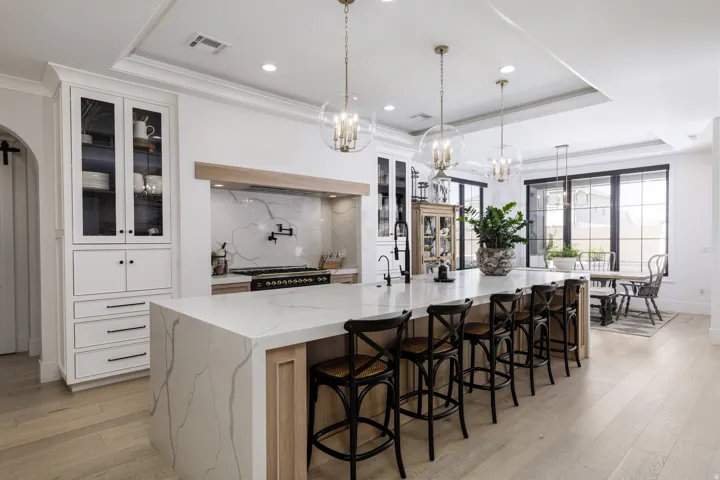Gourmet kitchen with a waterfall island, integrated range hood, white shaker cabinetry, pendant lighting, and wood-finish flooring
