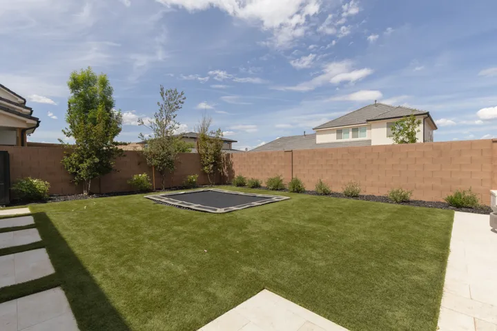 Expansive backyard featuring artificial turf, mature trees, a block privacy fence, and a patio with stepping stones