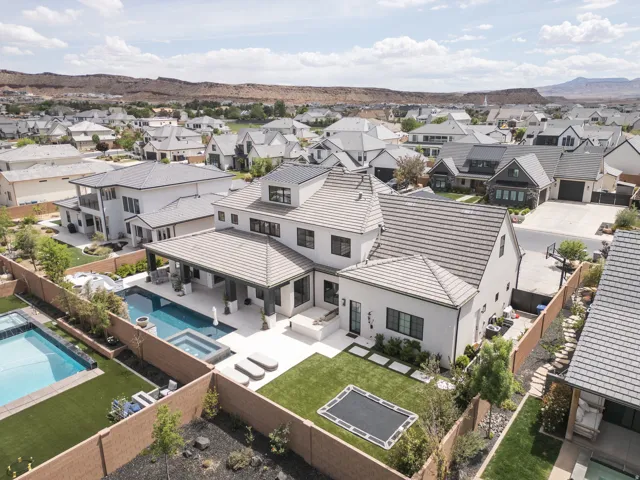 Contemporary residence featuring a multi-gabled roofline, expansive covered patio, outdoor swimming pool with integrated spa, and a landscaped backyard with turf