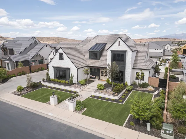 White brick exterior with dark trim accents, multi-level tiled roof, manicured front lawn, landscaped garden beds, and paver pathway