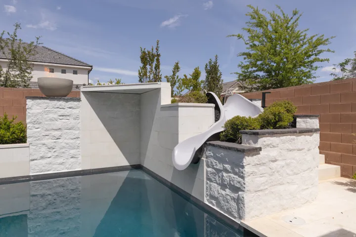 Swimming pool with stacked stone accents, integrated water slide, and a fire bowl feature