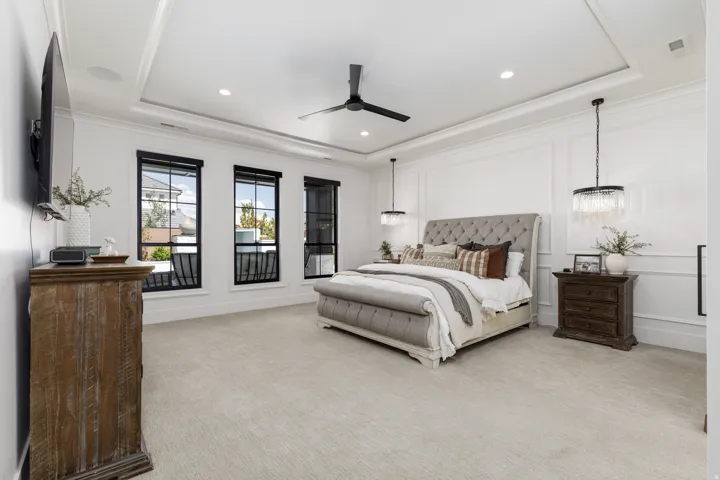 Tray ceiling with recessed lighting, crown molding, decorative wall paneling, three large windows with black frames, and a ceiling fan