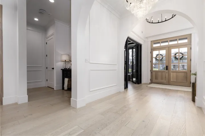 Light wood-finish flooring, white paneled walls, arched doorways, a double-door entry with transom windows, and an ornate chandelier