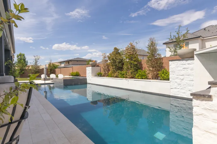 Swimming pool with a dark tile perimeter, light-colored paver decking, and a raised spa with a dark tile finish