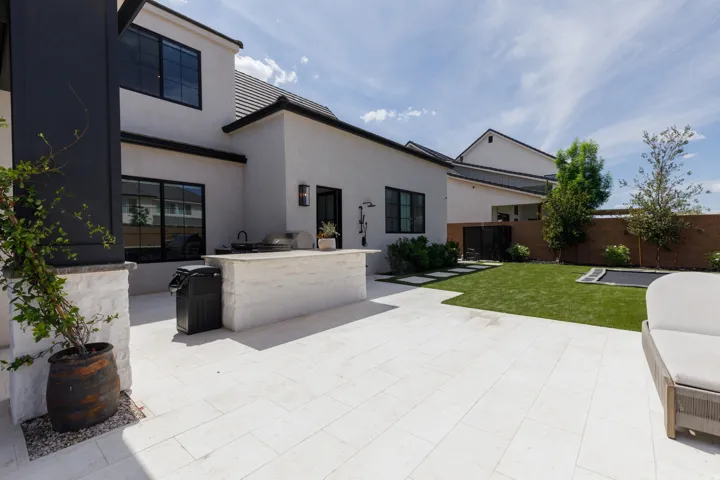 Expansive paved patio with an integrated outdoor kitchen, artificial turf lawn, and mature landscaping