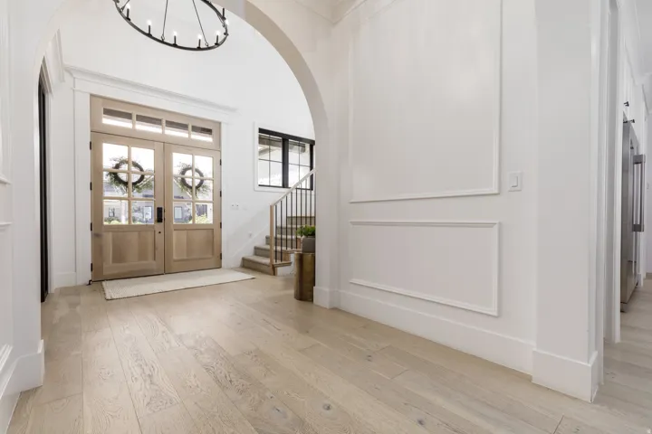 Grand entry featuring natural wood double doors with glass panels, high arched ceilings, a striking circular chandelier, elegant wall paneling, and light wood-finish flooring