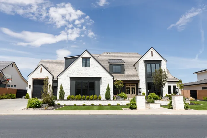 Modern Tudor exterior featuring white brick, dark framed windows, a light-toned tile roof, a double front entry door, and an integrated two-car garage