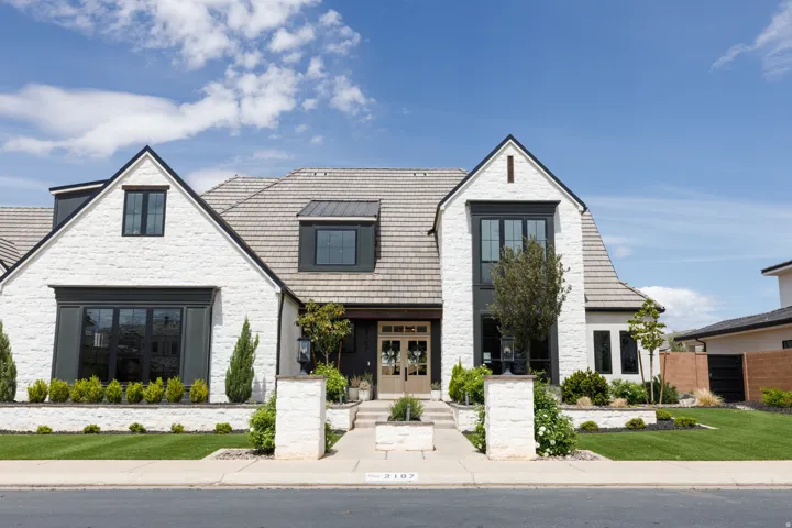 White brick exterior with dark trim windows, multi-gabled roofline, and stone tile roofing