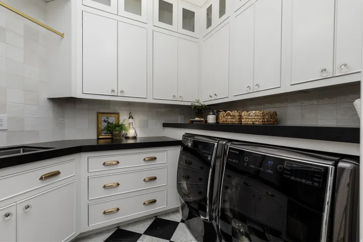 Laundry area featuring extensive white cabinetry, black countertops, a utility sink, a hanging rod, and checkerboard floor tiling