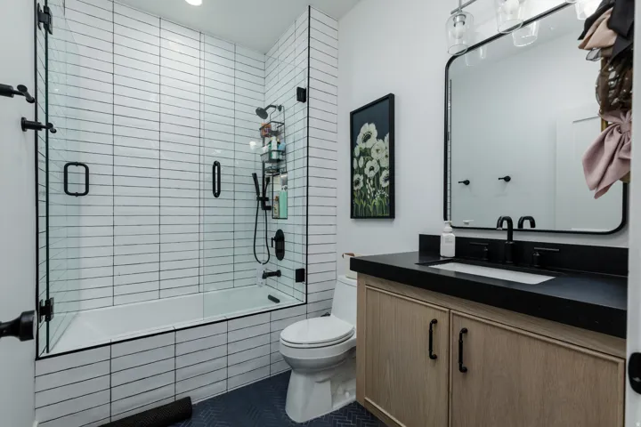 Full bathroom featuring a tub-shower combination with glass enclosure, horizontal subway tile surround, dark wood-finish vanity with a dark countertop, and a contemporary wall-mounted mirror