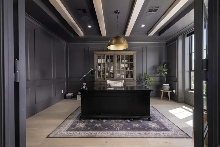 Light wood-finish flooring, dark paneled walls, exposed ceiling beams, recessed lighting, and a prominent brass pendant fixture
