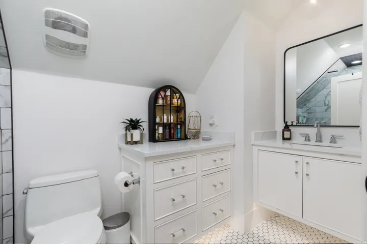 White hex tile flooring, built-in vanity with under-mount sink, white paneled cabinetry, white stone countertops, and a contemporary black-framed mirror