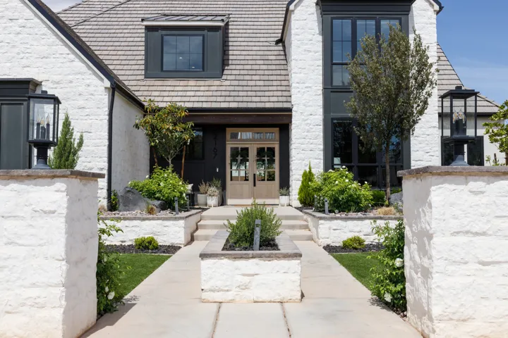 Stone exterior with dark-framed windows, a wood entry door, and a multi-level stone hardscape featuring integrated planters and exterior lighting