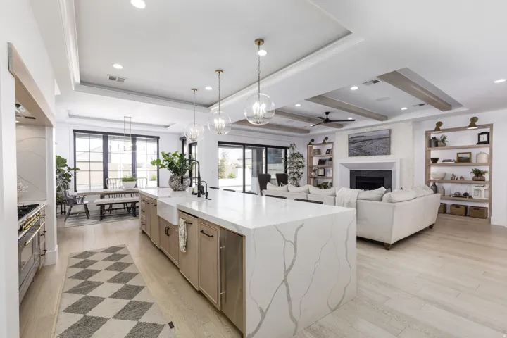 Gourmet kitchen island with an integrated farmhouse sink, light wood-finish cabinetry, and pendant lighting