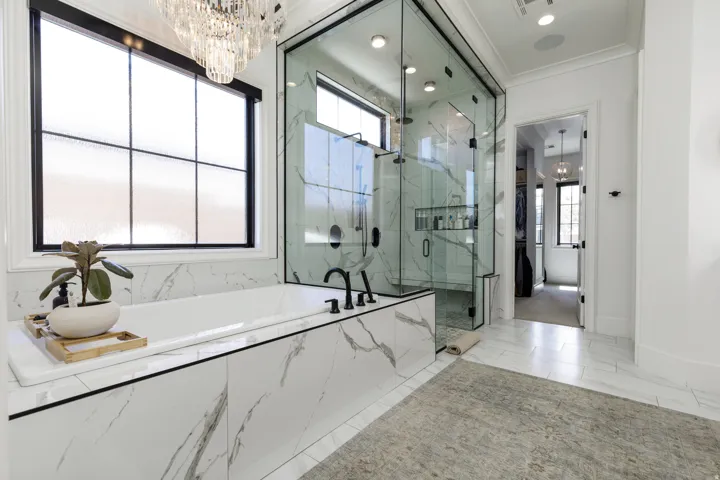 Freestanding soaking tub with matte black fixtures, marble-patterned tile surround, frameless glass shower enclosure, and a crystal chandelier