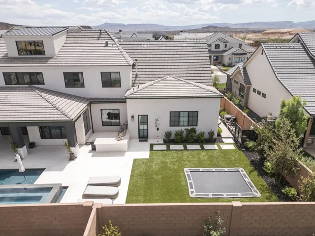 Multi-level residence featuring a tile roof, stucco exterior, rear patio, swimming pool, and an artificial turf lawn