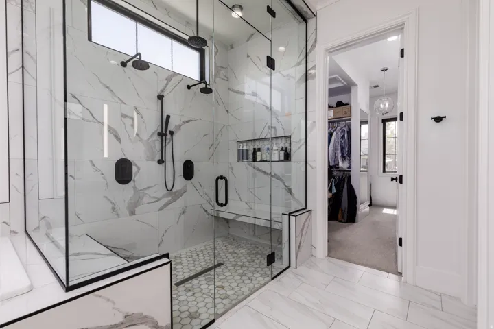 Spacious walk-in shower with dual shower heads, a built-in bench, hexagon tile flooring, and integrated shelving