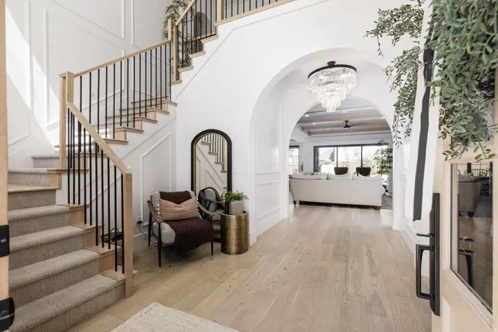 Grand entryway featuring light wood-finish flooring, a carpeted staircase with wood and metal railings, arched doorways, and elegant wall paneling