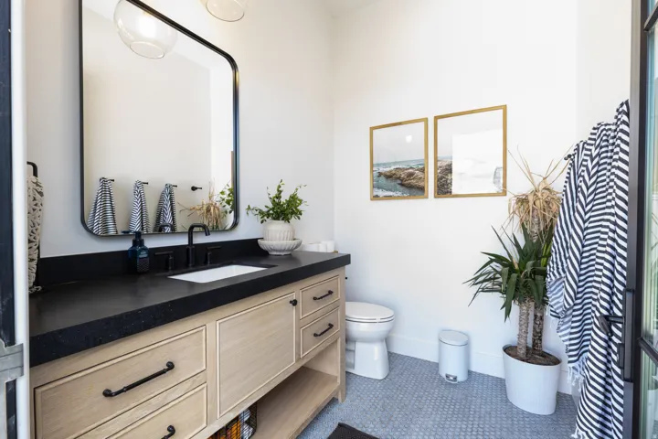 Pool Bathroom. Light wood-finish vanity with dark hardware, a black countertop, and an undermount sink.