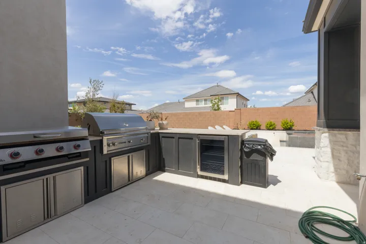 Outdoor kitchen featuring an integrated grill, flat-top griddle, under-counter refrigerator, and stainless steel cabinetry