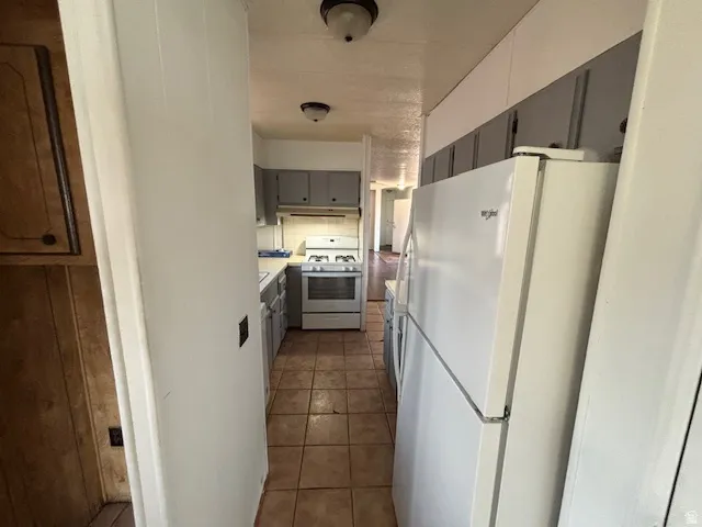 Galley kitchen with tile flooring, white appliances, and gray cabinetry