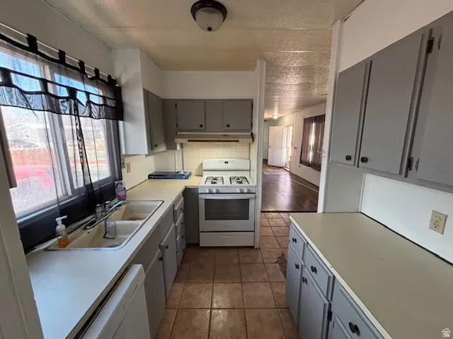 Galley kitchen featuring a gas range, dual-basin sink, upper and lower cabinetry, and tile flooring