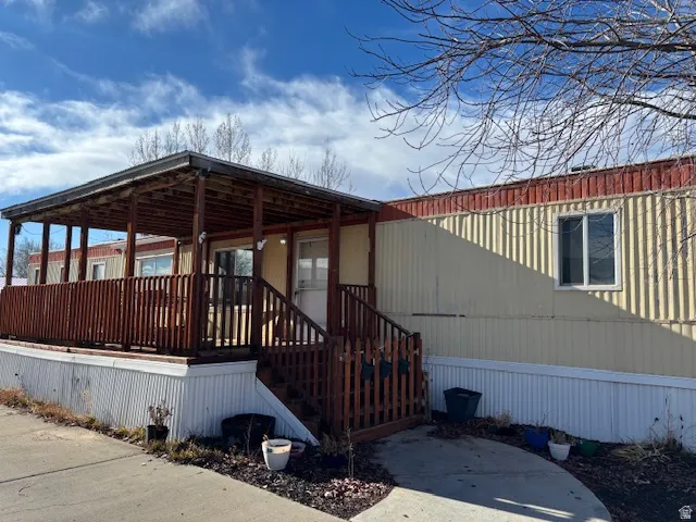 Covered wood deck with railings, wood steps, and a concrete walkway