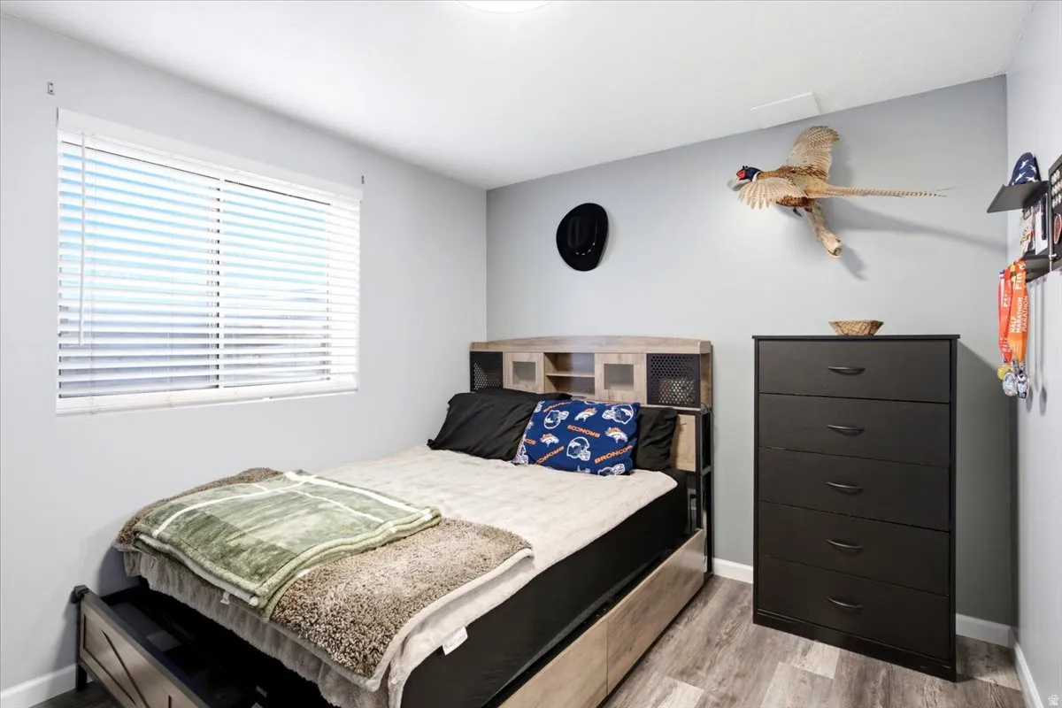 Light gray walls with a horizontal window featuring white blinds, wood-finish flooring, and a built-in light fixture