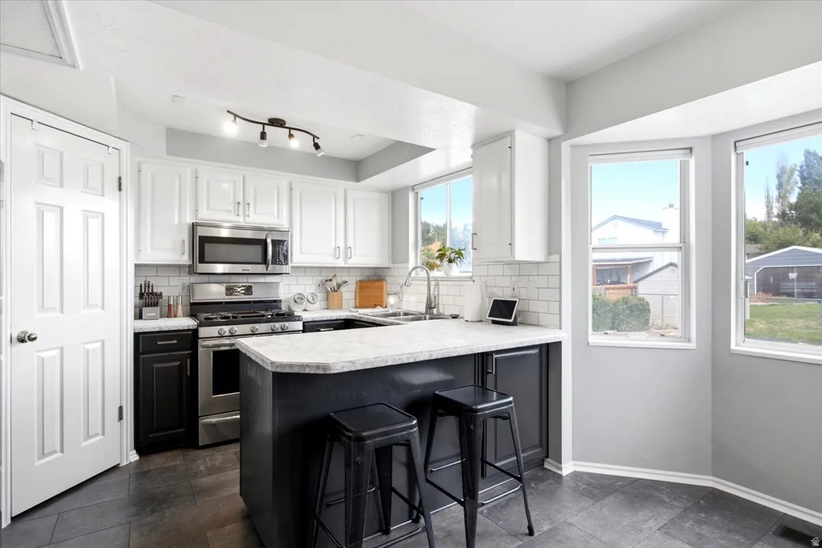 Kitchen featuring a central island with countertop seating, stainless steel appliances, white subway tile backsplash, and a corner bay window