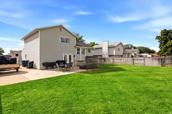 Expansive green lawn, concrete patio, double French doors, and wood fence