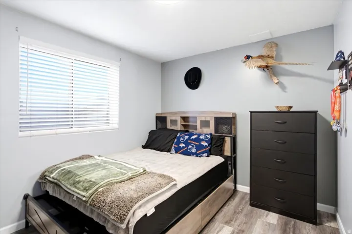 Light gray walls with a horizontal window featuring white blinds, wood-finish flooring, and a built-in light fixture