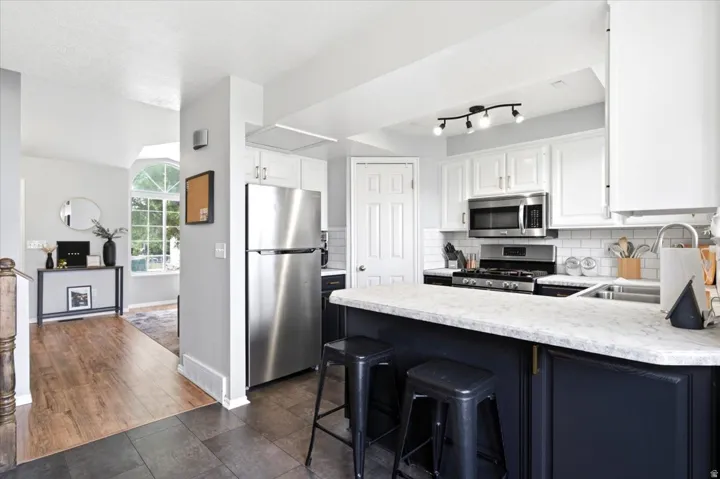 Kitchen featuring white upper cabinetry, dark lower cabinetry, stainless steel appliances, and a peninsula with a light-toned countertop