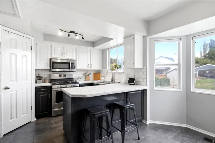 Kitchen featuring a central island with countertop seating, stainless steel appliances, white subway tile backsplash, and a corner bay window