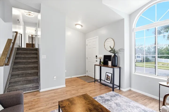 Wood-finish flooring, staircase with carpeted treads and wood handrail, arched top window with grid pattern, white paneled door, and recessed lighting