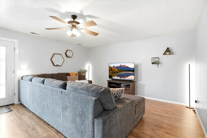Wood-finish flooring, ceiling fan with integrated lighting, white walls, and a glass-paneled exterior door