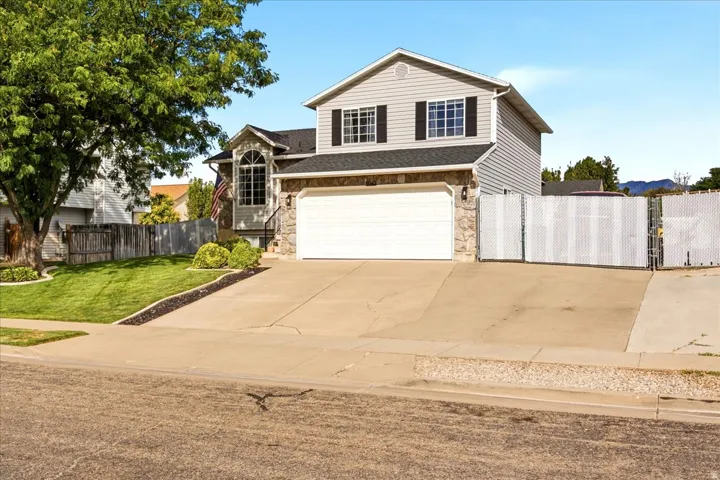 Two-story residence featuring light gray siding with stone-clad accents, a two-car garage, and a fenced side yard