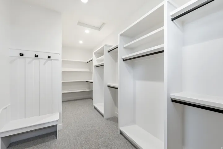 Built-in white shelving, black hanging rods, white beadboard paneling, built-in bench seating, and recessed lighting