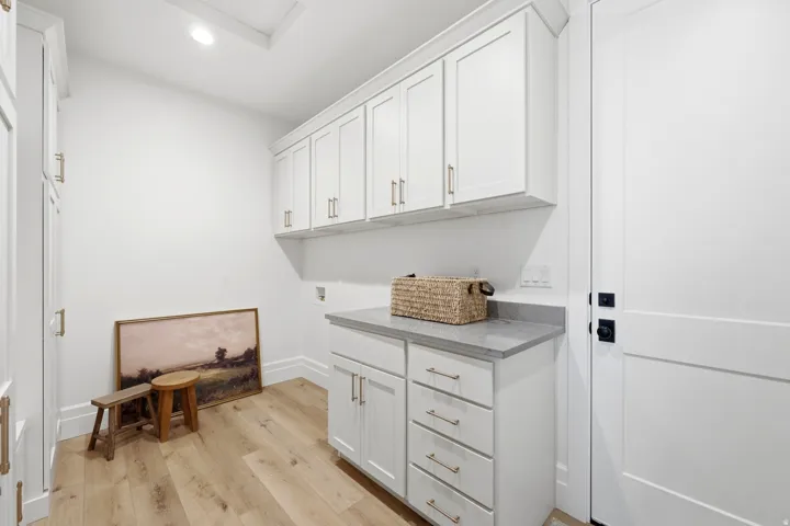 White shaker cabinetry, light wood-finish flooring, light gray countertop, matte black door hardware, and recessed ceiling lighting