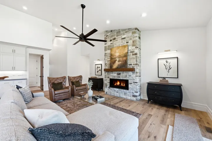 Vaulted ceilings, wood-finish flooring, stone-clad fireplace with a wood mantle, recessed lighting, and a modern ceiling fan