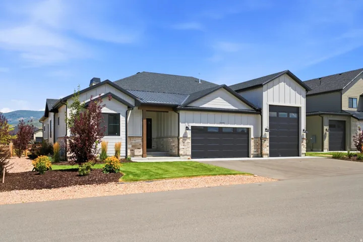 Modern farmhouse exterior featuring board and batten siding, stone accents, dark-framed windows, and a multi-car garage with contemporary doors