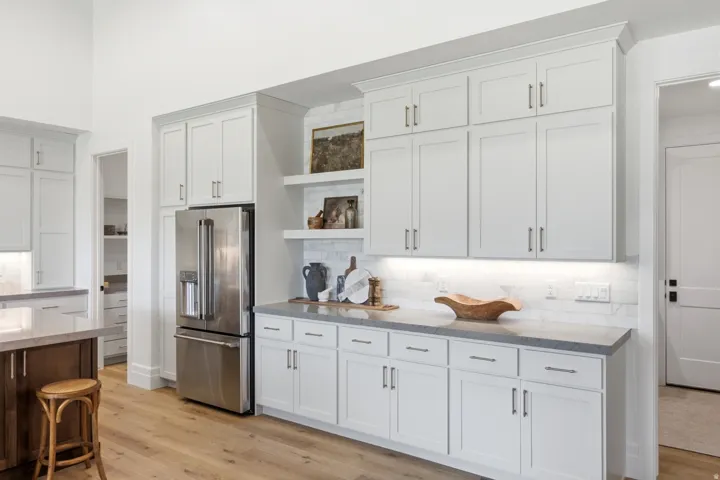 White shaker-style cabinetry, wood-finish flooring, stainless steel refrigerator, stone countertops, and a subway tile backsplash