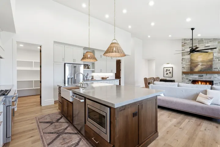Open-concept kitchen and living area featuring a central island with integrated sink and microwave, wood-finish flooring, a stone-clad fireplace, and recessed lighting