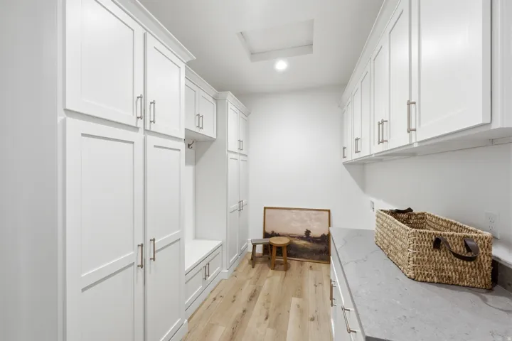 White shaker-style cabinetry with brushed nickel hardware, built-in storage bench, wood-finish flooring, recessed lighting, and a skylight