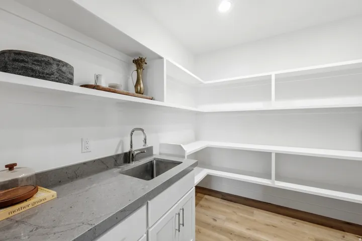 Extensive built-in shelving, wood-finish flooring, undermount sink with a gooseneck faucet, built-in cabinetry, and a stone-finish countertop