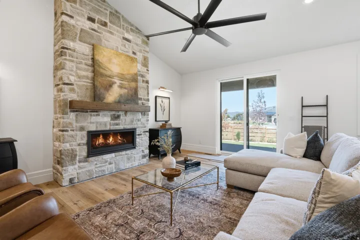 Vaulted ceiling featuring a large ceiling fan, stone fireplace with a wood mantel, built-in linear fireplace, wood-finish flooring, and sliding glass doors