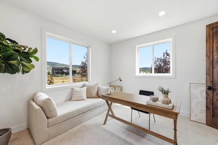 White walls, recessed lighting, two white-framed windows, wood-finish door with black hardware, and neutral-toned carpeting