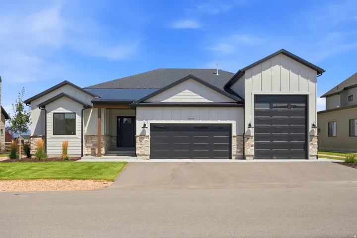 Contemporary exterior featuring light siding, stone accents, a dark roof, and a three-car garage
