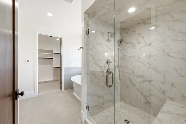 Glass-enclosed shower with marble-finish tile walls and a built-in bench