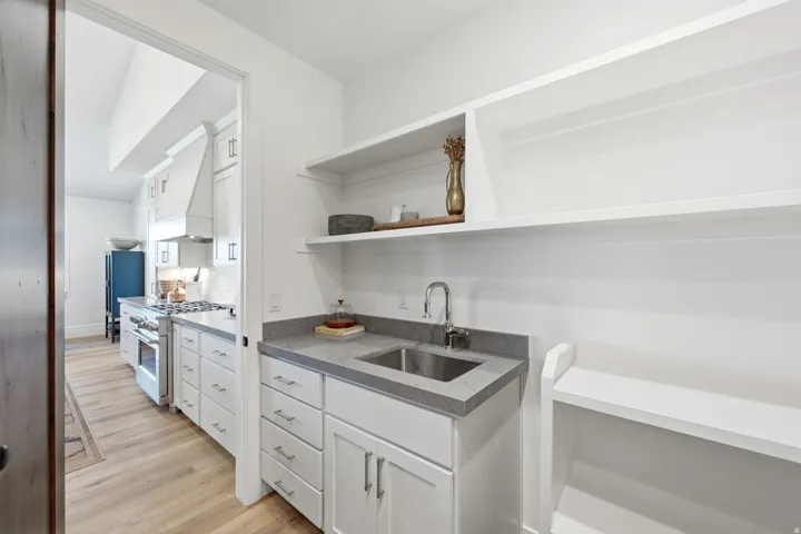 Pantry featuring open shelving, white cabinetry with silver hardware, an undermount sink, and a gray countertop